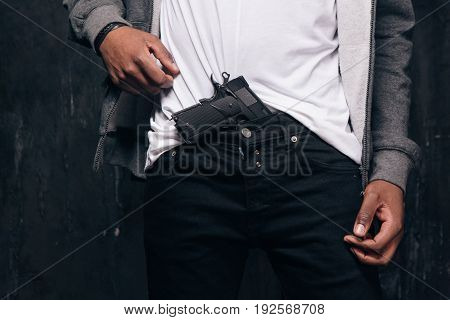 Unrecognizable black man threatens with a gun closeup studio shoot. Ghetto gangster with weapon on dark background. Outlaw, ghetto, murderer, robbery concept
