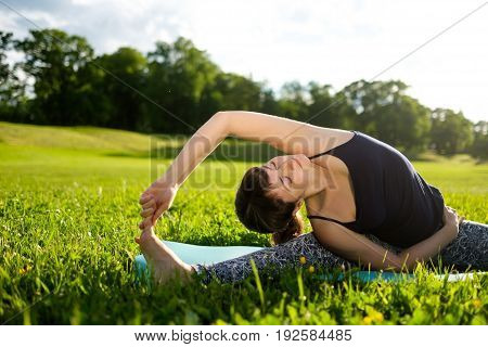 Woman practices balance yoga asana Vrikshasana tree pose in parkoutdoors in the morning.