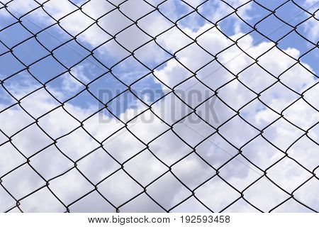Metallic fence against the blue sky with clouds.Net metallic pattern barrier against blue sky. Chain Link Fence against  Cloudy Blue Sky.