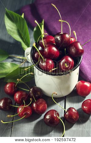 Ripe cherries in an iron mug on a dark blue wooden background. With copy space.