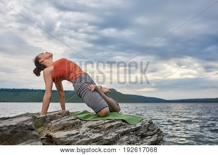 Young sporty woman doing different variants of yoga position on a rocky rivershore. Beauty woman dressed in the sportwear and barefoot. Beautiful landscape like a background. Concept of the healthy and active lifestyle.