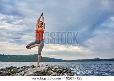 Young sporty woman doing different variants of yoga position on a rocky rivershore. Beauty woman dressed in the sportwear and barefoot. Beautiful landscape like a background. Concept of the healthy and active lifestyle.