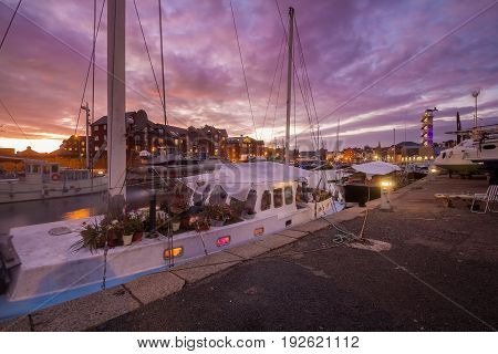 Yacht in the harbor. On board the yacht there are a lot of pots with flowers. Inside the light is on. Beautiful sunset. Exeter. Devon. England