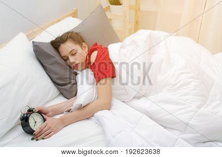 A asian young woman in red pajamas sleeping on bed and alarm clock in bedroom at the morning selective focussunlight effect