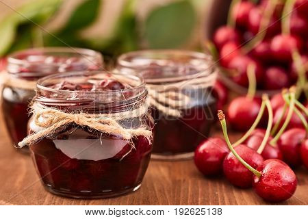 Cherry jam on wooden background in glass jars