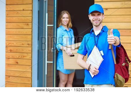 Smiling delivery man in blue uniform delivering parcel box to recipient - courier service concept