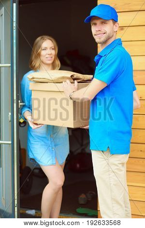 Smiling delivery man in blue uniform delivering parcel box to recipient - courier service concept