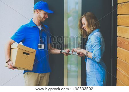 Smiling delivery man in blue uniform delivering parcel box to recipient - courier service concept