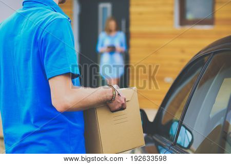Smiling delivery man in blue uniform delivering parcel box to recipient - courier service concept