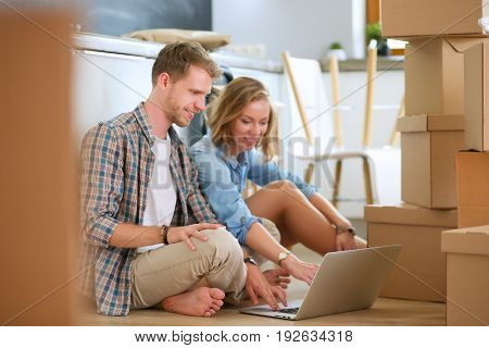 Young couple moving in new home.Sitting on floor and relaxing after unpacking.Looking something on laptop