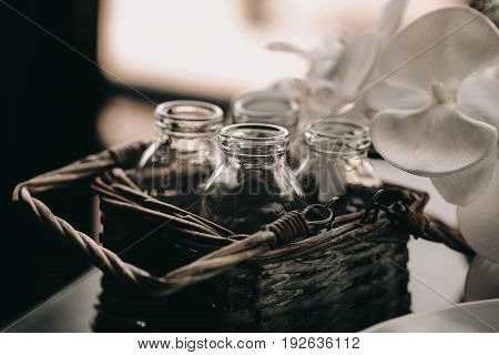 Glass Bottle in vintage Wicker basket. Decor box in loft interior. Flower blurred blackground. Vintage toning photo.