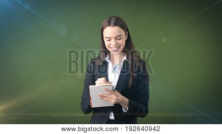 Friendly Confident Smiling Businesswoman Writing In Her Organizer Isolated On Studio Background.