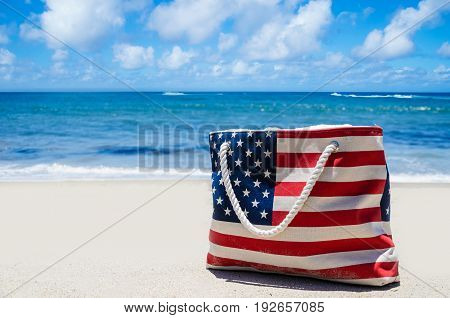 Bag with American flag colors near ocean on the sandy beach - USA patriotic holidays background
