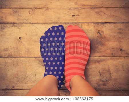 Selfie feet wearing blue sock with white star shape and red one wth white striped on wooden floor background vintage filter effect. American flag and 4th of July concept.