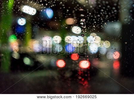 Night city life through windshield : Drops of rain on car's mirror upon traffic jam.