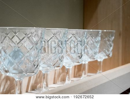 Decorative crystal glasses in a row on wooden shelf. Home interior design for background.