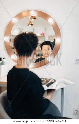 Attractive woman primp at the mirror with lamps in the beauty studio. A happy satisfied customer of make-up and hairstyle service.