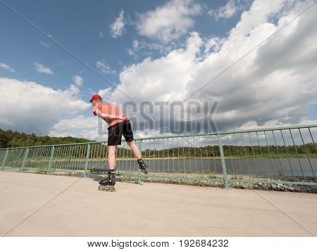 Roller Skater In Action. Man Ride In Inline Skates Ride Along Promenade Handrail, Sky In Background