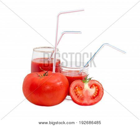 Big fresh whole tomato with bendable drinking straw inserted into it half of the tomato and two different glasses with tomato juice and drinking straws on a light background