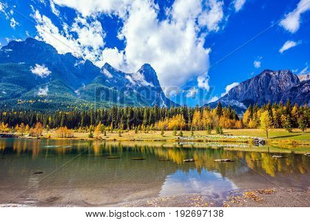  The concept of recreational tourism. Path around the lake. Canmore, near Banff National Park. Majestic mountains and scenic cumulus clouds are reflected in the water
