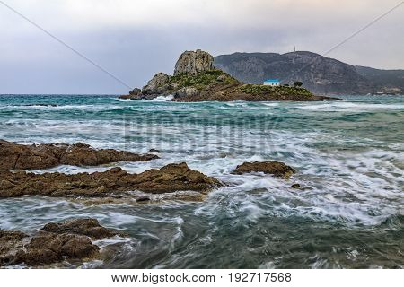 Dramatic scene of rocks washes of stormy sea with small island Kastri in Kos Greece.