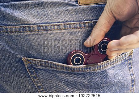 Caucasian man hides his red finger fidget spinner at jeans pocket. Popular spinner gadget in 2017.