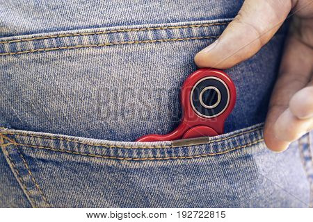 Caucasian man hides his red finger fidget spinner at jeans pocket. Popular spinner gadget in 2017.