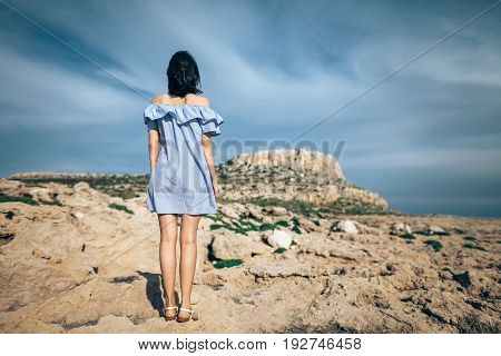 Back view of lonely woman standing on rocky desert with dramatic sky