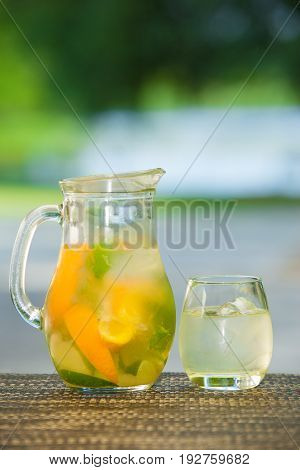 Jug of non-alcoholic drink and a glass of ice on a table with a blurred background.