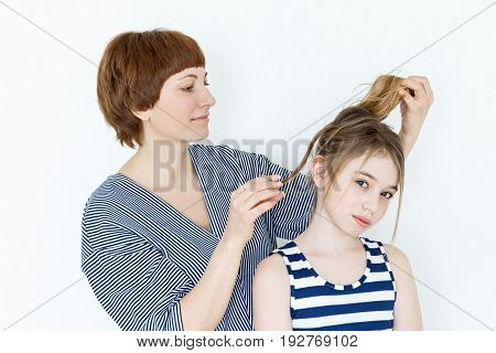 Mother and daughter playing with blond long hair near white wall