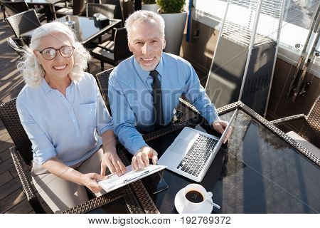 We are group mates. Friendly partners sitting next to each other while keeping hands on the folder and being on the terrace