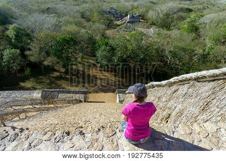 Tourist sitting on the pyramid looking down on the ruins of the ancient Mayan city of Ek Balam near Valladolid Mexico