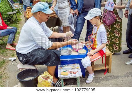 Zaporizhia/Ukraine- May 28, 2017: Charity Family festival:  Outdoors pottery workshop - ceramist master explaining to girl how to cut a piece of clay with a string. Art and craft activity.