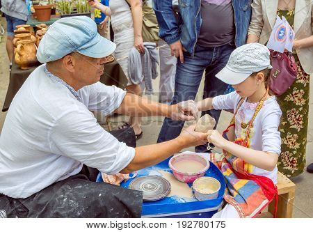 Zaporizhia/Ukraine- May 28, 2017: Charity Family festival:  Outdoors pottery workshop - ceramist master helps girl to cut a piece of clay with a string. Art and craft activity.