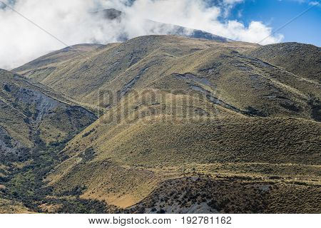 Middle Earth New Zealand - March 14 2017: High mountain range with top in clouds at Rock of Middle Earth under blue sky with white clouds. High desert mountainous scenery. Shale pebble flow off top.