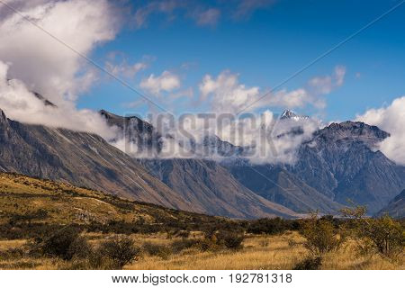 Middle Earth New Zealand - March 14 2017: Snow capped High mountain range around Rock of Middle Earth under blue sky with white clouds. Set in a high desert mountainous scenery.