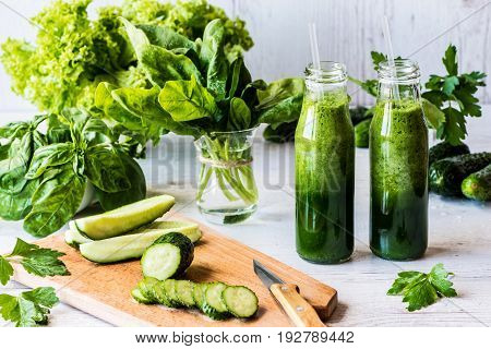 Detox diet. Two small bottles of fresh green smoothies with ingredients on a light wooden background