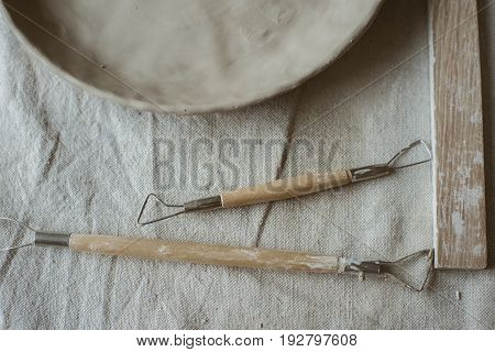 Pottery tools with wooden holders and raw clay plate on table with industrial fabric in pottery studio