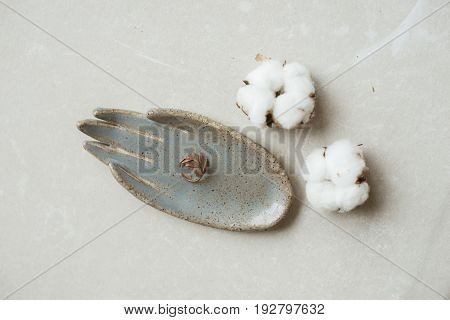 Top view on chamotte clay blue and grey rustic hand holding beautiful twig ring on grey industrial table with flowers of cotton