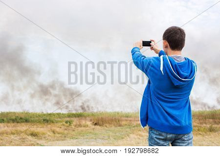 the man filming strong smoke over the burning fields of ripe wheet during the strong heat and a drought in the summer.