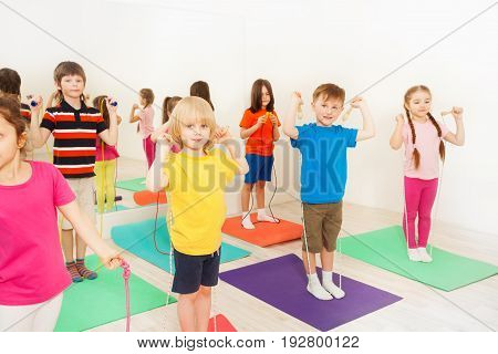 Group of 5-6 years old kids standing in two lines and jumping with skipping rope in gym