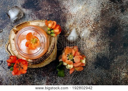 Floral pastel peach and pink brunch cocktail garnished with quince flowers over old rustic background. Top view flat lay copy space
