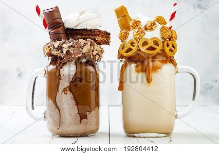 Caramel and chocolate indulgent exreme milkshakes with brezel waffles popcorn marshmallow ice cream and whipped cream. Crazy freakshake food trend.