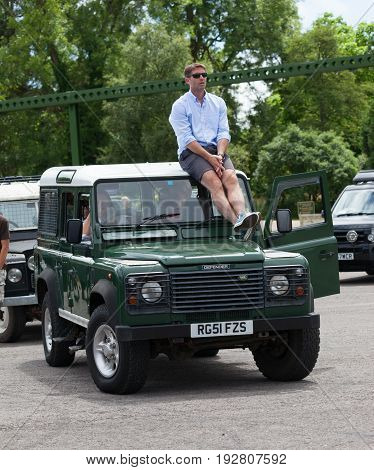 BEAULIEU HAMPSHIRE UNITED KINGDOM - JUNE 25 2017 Land Rover day with many varieties of Land Rovers including this green Land Rover Defender with a man sitting on the roof waiting in queue of Land Rovers.
