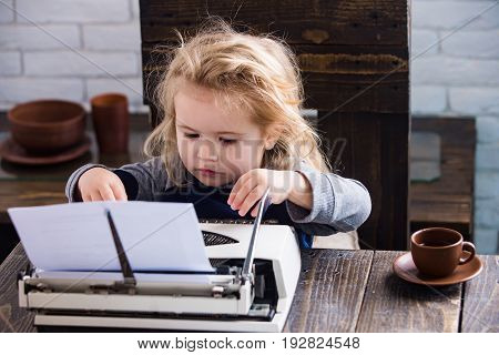 kid or small businessman child sitting at table and typing typewriter with paper and coffee cup on white brick wall background business and new technology