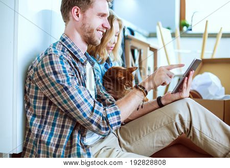 Young couple moving in new home.Sitting on floor and relaxing after unpacking.Looking something on laptop