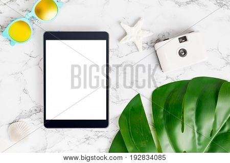 Blank Screen Tablet Computer On Marble Table Top View With Summer Beach Accessories And Monstera Lea