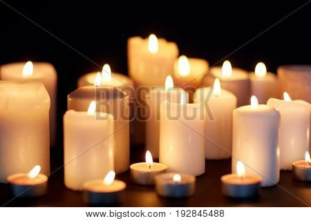 mourning and commemoration concept - candles burning in darkness over black background
