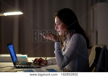 business, technology, overwork, deadline and people concept - woman with laptop and smartphone using voice command recorder at night office