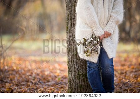 Woman standing near the tree and holding seasonal bouquet in her hands on a sunny autumn day in the park. Girl walking in the park and enjoying autumn. Lifestyle and autumn concept